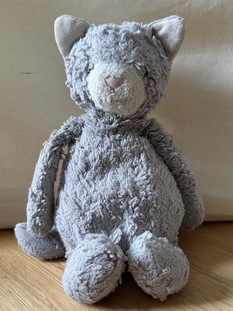 A well-loved plush cat sitting on the floor against a sofa.
